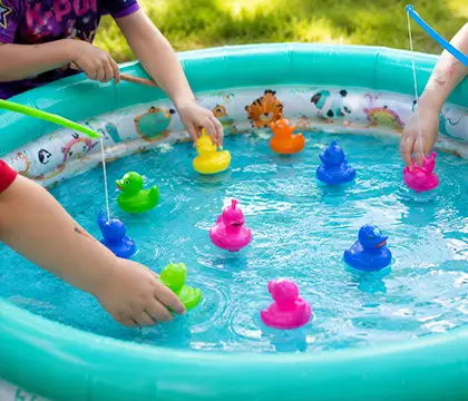 Kinderhände spielen mit bunten Enten in einem kleinen Planschbecken.